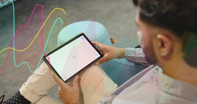 Vertical video: Adult Indian man on blue sofa with tablet tracing screen as neon overlays appearing
