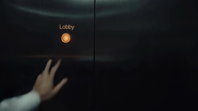 A hand in a formal shirt pressing the elevator button for the lobby, reflecting a sleek, metallic interior