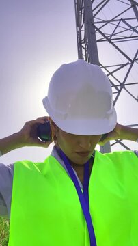 Female powerline technician wearing safety gear while inspecting a high voltage transmission tower