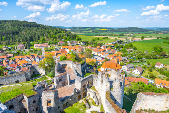 The view from the lookout at Rabi Castle shows the castle ruins and the nearby village. The landscape is green with fields and houses. Clouds are present in the sky.