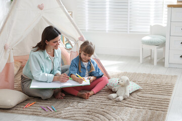 Mother and her daughter drawing in sketchbook together near toy wigwam at home, space for text © New Africa