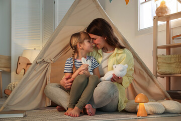 Mother and her daughter with toys near wigwam at home © New Africa