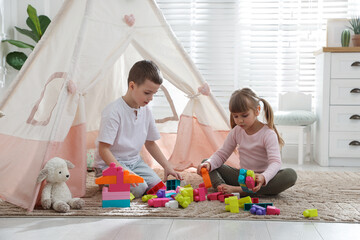 Little kids playing with building blocks near toy wigwam at home © New Africa