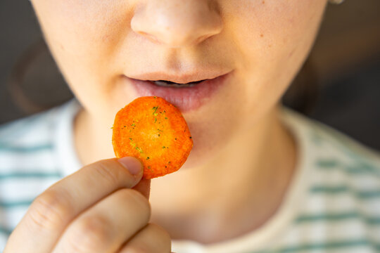 Woman eating carrot chip as healthy snack at home. Clean eating and mindful diet concept with natural vegetable chips.
