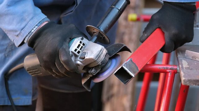 A worker in protective gloves is processing metal with an angle grinder, sparks fly. Production, repair, construction, industry, labor safety.