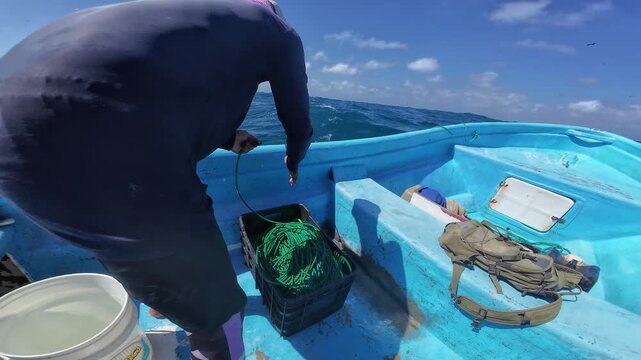 Hardworking fisherman meticulously organizes green ropes and artisanal gear on a blue boat amidst the choppy Caribbean waters.