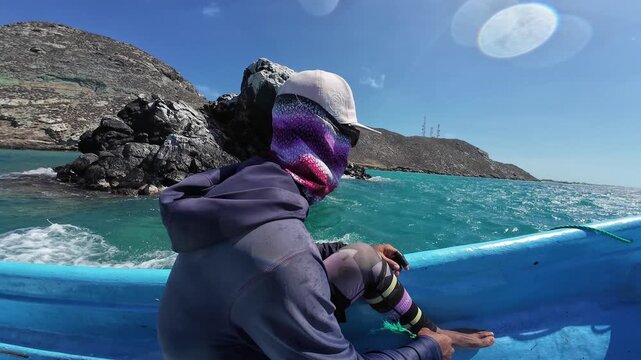 Cinematic profile of a fisherman on a moving boat, capturing the vibrant turquoise sea and dramatic rocky coastline of a tropical island.