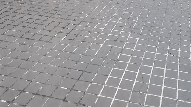 Video of concrete pavement tiles arranged in grid pattern forming textured outdoor walkway surface