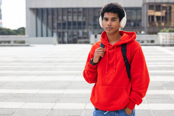 Obraz premium African American man standing on tiled plaza by building wearing red hoodie, backpack, copy space