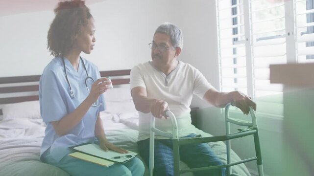 Nurse sitting bedside lifting med cup, tapping clipboard, explaining meds to senior holding walker