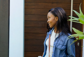 Fototapeta premium African American woman standing by wood-paneled door, wearing denim, holding bottle, copy space