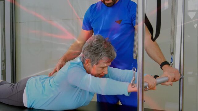 Senior woman performing guided shoulder pulls on pulley unit, trainer cueing pull for rehab support
