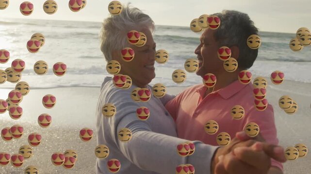 Senior couple holding hands, dancing on beach, emoji cascade starting from left for marketing