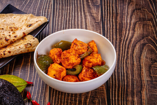 Indian Paneer Tikka Masala inl with Roti bread on a dark wooden table
