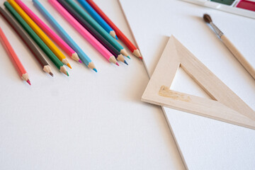 Obraz premium Assorted wooden pencils, drafting triangle, paintbrush, and blank canvas arranged on a white surface, representing the preparatory stage of analog artistic creation