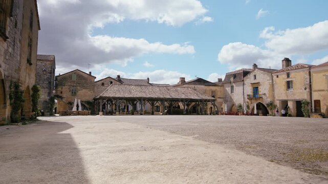 Historical town square with its traditional wooden market hall in Monpazier, Dordogne. Old stone buildings line the plaza. Slow motion traveling shot.