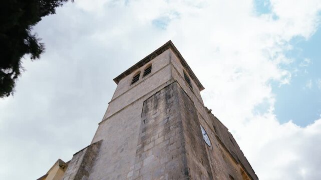 Stone facade of a medieval clock tower in Monpazier, Dordogne, looking up from the ground level. Slow motion tracking movement.