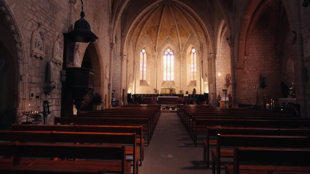 Interior of the Gothic church featuring wooden pews and stone arches in Monpazier, Dordogne. The view looks toward the altar. Slow motion movement.