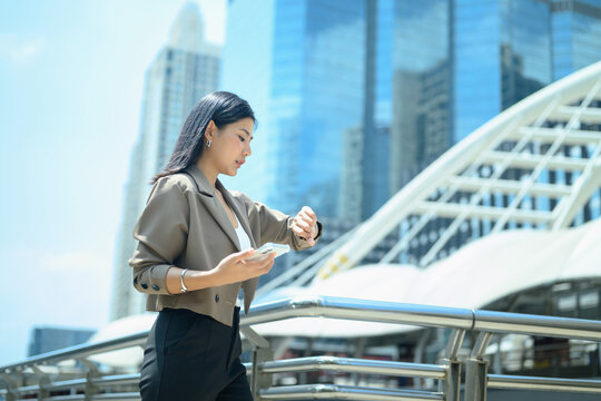 Adult businesswoman standing on an urban walkway, checking her smartwatch rush hour
