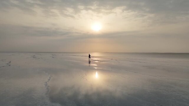 Aerial view of the salt flats in the Danakil Depression, where vast white mineral crusts stretch across Ethiopia&rsquo;s Afar region. Person running in the shallows on the flats. Drone shot Into the sun.