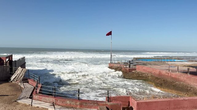 Powerful ocean waves hitting a coastal promenade during a storm, with Morocco flag waving, tc01