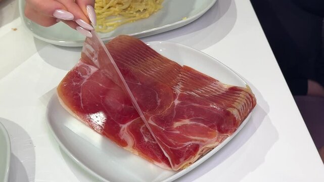 Person puts delicious serrano ham on a wooden plate