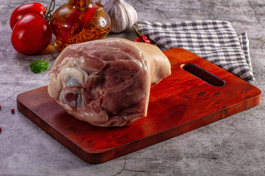 Raw pork knuckle on a wooden cutting board with vegetables and spices