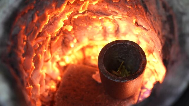 Goldsmith melting gold pieces inside a high-temperature furnace using a crucible. Shows goldsmithing process, metal melting stage and traditional jewelry production in workshop environment.