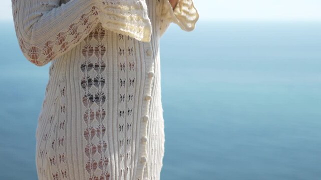 Woman, unbuttoning, cardigan, female unbuttons white knitwear by calm blue sea on sunny day.