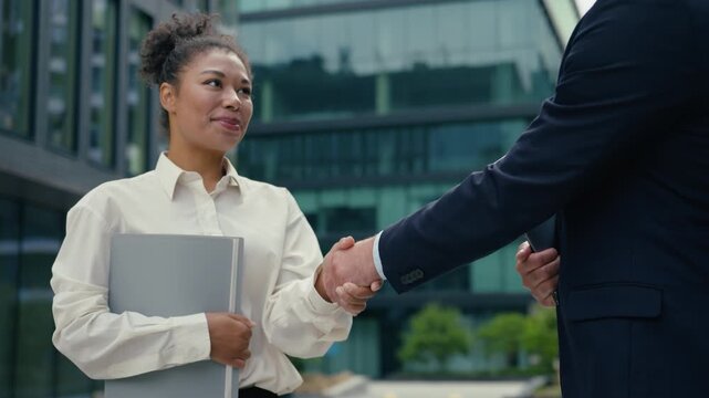 Business handshake African businesswoman female intern holding folder smiling shaking hands Caucasian businessman male multiracial managers outside city partnership hiring recruitment teamwork deal