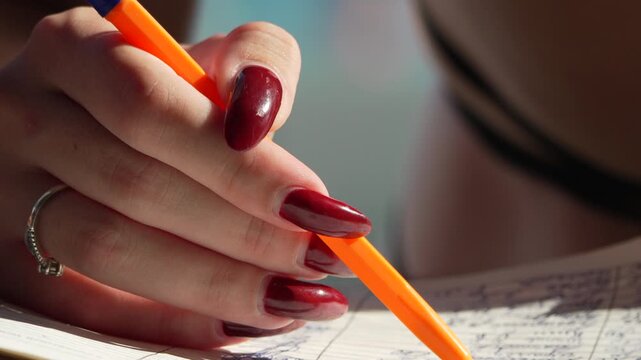 Hand writing pen, woman's hand with red nails writing in a notebook, focused close-up shot