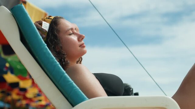 Serene woman resting under colorful umbrella. Tranquil scene of lady lounging by vibrant ocean setting. Peaceful vacation scene with woman resting on beach chair beneath bright umbrella