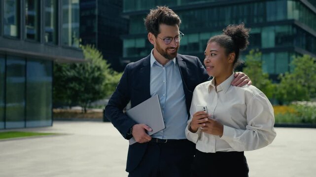 African American business woman walking in city using mobile phone chatting Caucasian businessman approaching hugging female multiethnic coworkers meeting outdoors talking harassment awkward outside