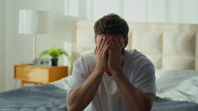 Angry Caucasian man at home bedroom throwing smartphone on bed bad news irritated European male guy technology error failure trouble furious bankruptcy loss touching face frustration crisis indoors