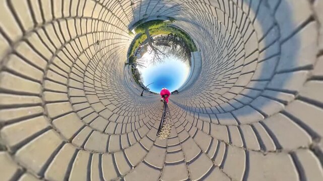 Cycling path journey, woman rides bicycle in abstract tiny planet view through a park on a sunny day