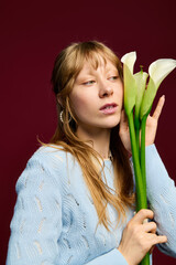 Naklejka premium Young woman embraces elegance with calla lilies against a rich burgundy backdrop