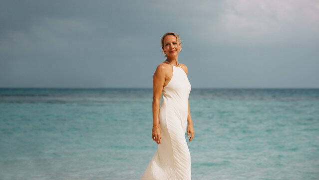 Woman in white dress standing on a tropical beach with blue waters