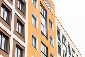 Obraz premium Modern building facade with colorful, geometric window patterns. Orange and beige walls contrast sharply against white sky. Clean lines and structured design suggest urban sophistication