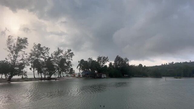 lone house, trees and palms sits on a sandbank beneath a sky of thick gray clouds.