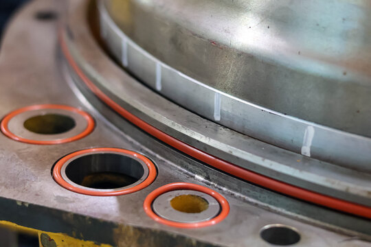Close up of orange rubber O-ring seals installed on a heavy industrial metal flange during a machinery maintenance and assembly process in a workshop for leak prevention.