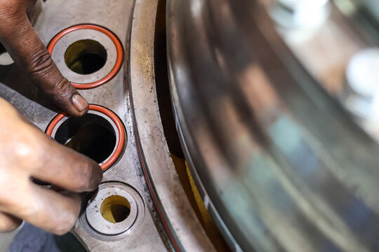 Close up of a mechanic installing orange rubber O-ring seals into a heavy metal industrial engine component in a workshop during a professional machinery maintenance.