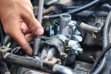 Fototapeta premium ​A mechanic uses a T-handle socket wrench to tighten bolts on a motorcycle engine intake manifold while installing a new carburetor in a workshop, ensuring a secure and leak-free fuel system.