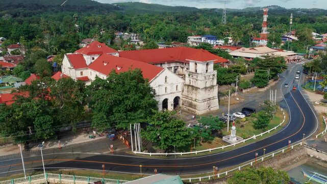 Aerial view of Baclayon Church complex with red roof buildings and curved road surrounded by tropical trees Bohol Philippines, drone