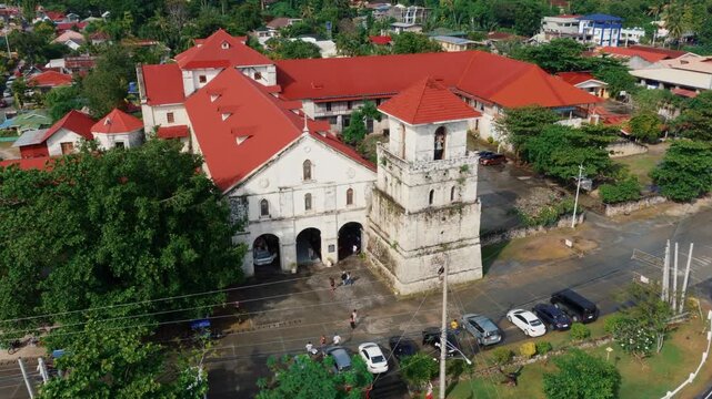 Aerial view of Baclayon Church with red roof buildings and bell tower surrounded by tropical town Bohol Philippines, drone