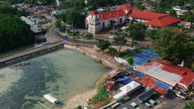 Aerial view of Baclayon Church beside coastal water and road with town buildings Bohol Philippines, drone