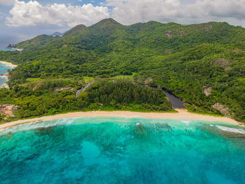Aerial view of turquoise waters meet the sandy beach and lush green forests of Mahe Island, a tropical paradise under a cloudy sky, Police Bay, Mahe Island, Seychelles.