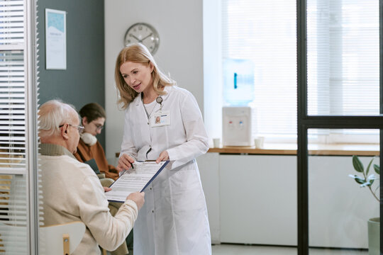 Caucasian female doctor explaining medical form to senior male patient in clinic, supporting informed care and treatment decisions. Useful for healthcare services, patient communication campaigns