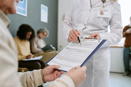 Senior patient receiving medical intake form from female doctor in clinic, completing registration before appointment. Useful for healthcare access, patient onboarding, insurance concepts