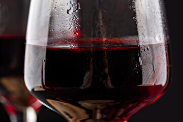 Fototapeta premium Grapes wine. Close-up view of glass filled with red wine, highlighting its deep color and clarity, with condensation visible on surface, set against dark background for contrast
