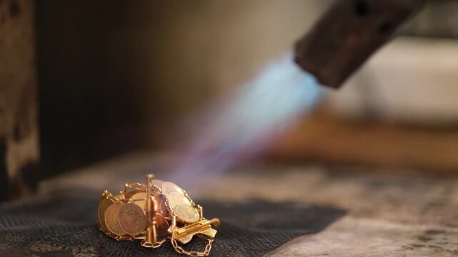 Close-up of a gold jewelry piece being soldered with a torch flame. Highlights traditional craftsmanship, heat processing and precision metalworking in a professional jewelry workshop.